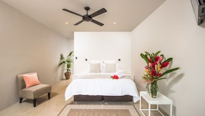 Quarto com cama, poltrona, mesa de cabeceira, planta e ventoinha no teto.