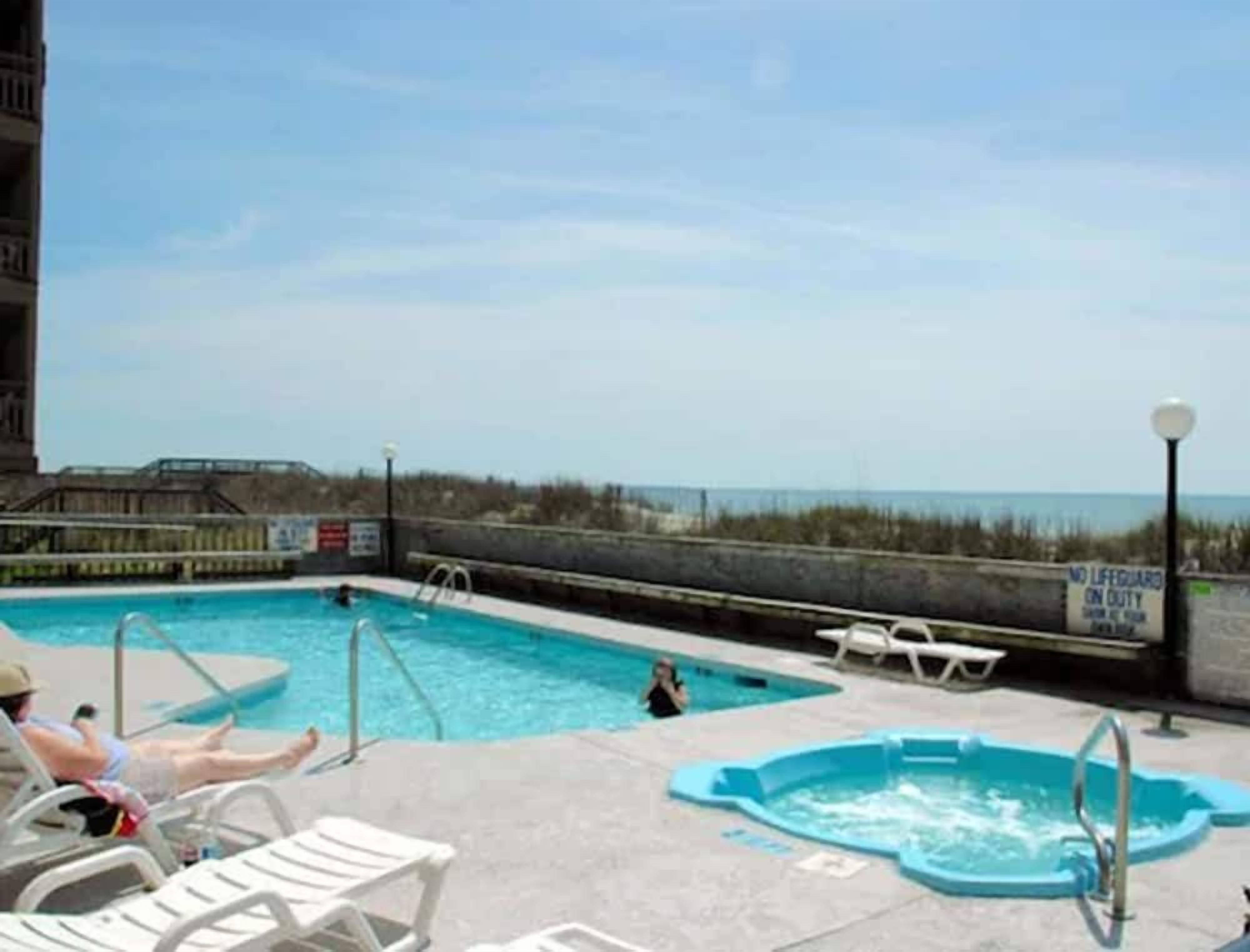 A pool area with a view of the beach, a lifeguard sign, and lounge chairs.