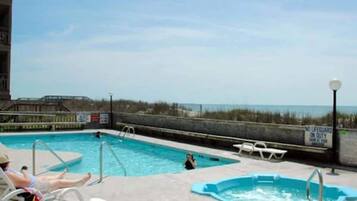 A pool area with a view of the beach, a lifeguard sign, and lounge chairs.