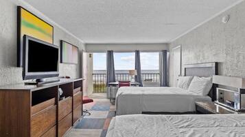A hotel room with two beds, a television, a desk, and a balcony with a view.