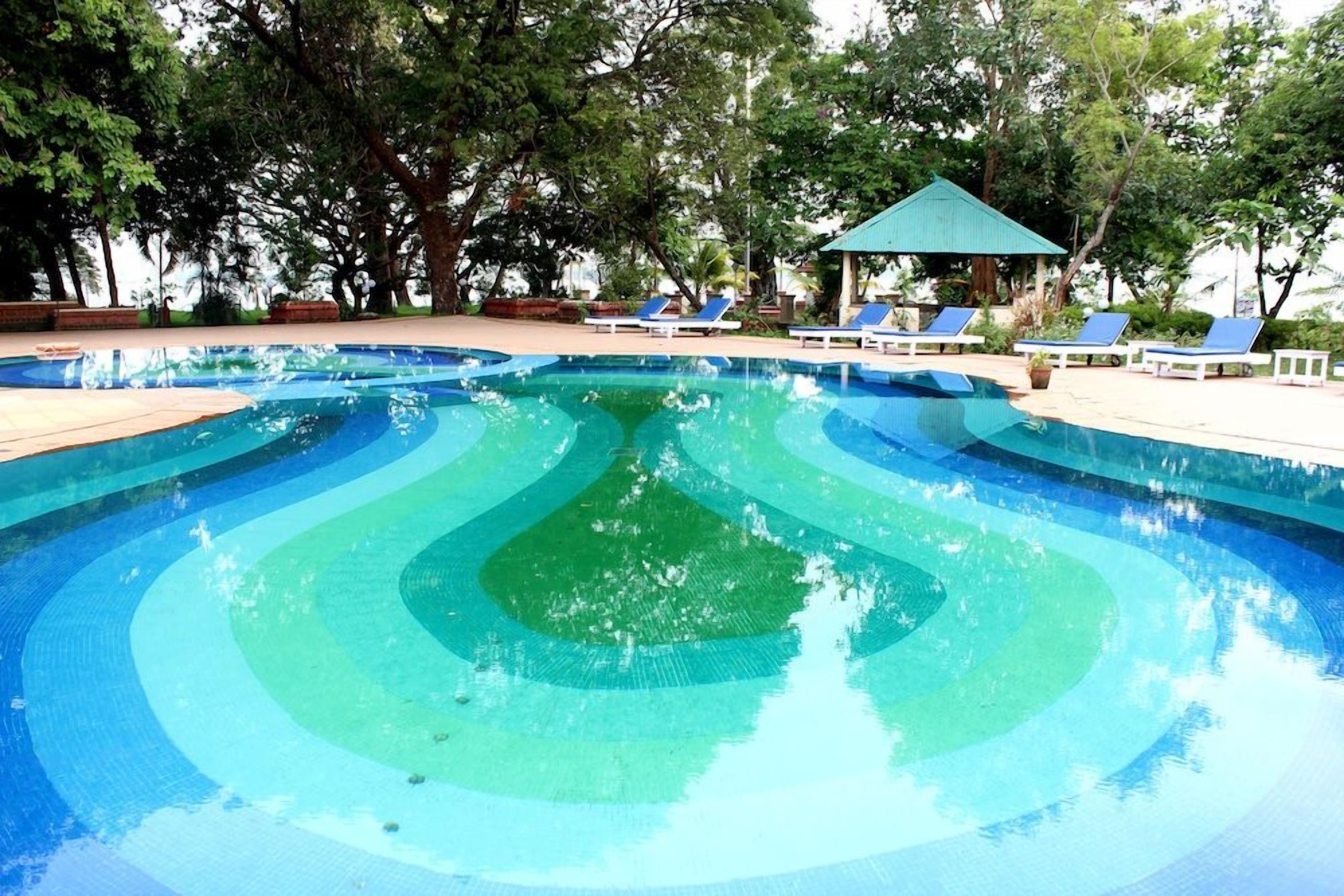 A swimming pool with a tiered design, surrounded by lounge chairs and a gazebo.