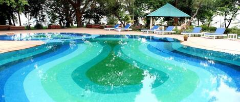 Una piscina con diseño escalonado, rodeada de sillas de descanso y un pabellón.