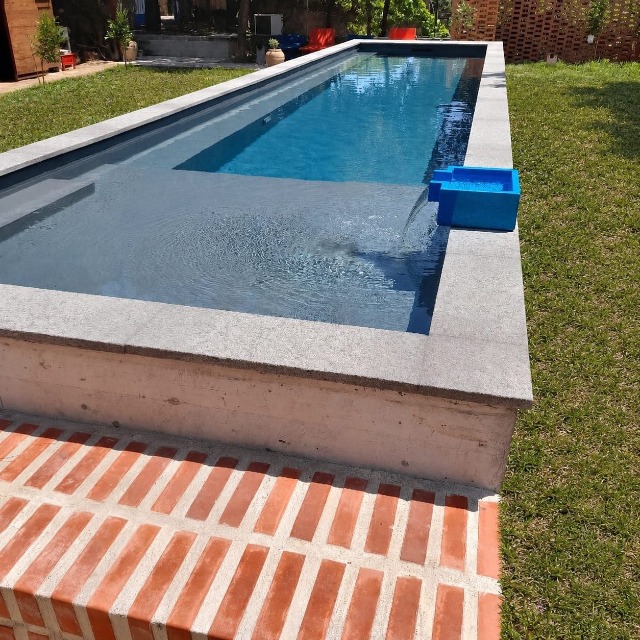 Piscina retangular com borda de concreto, rodeada por um pátio de tijolos e gramado.