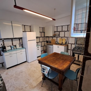 A compact kitchen with white cabinets, a wooden table, and blue chairs. - Chalet di Târa: 1970s-era villa with a private pool, within walking distance of the beach, and pet-friendly (Anzio)