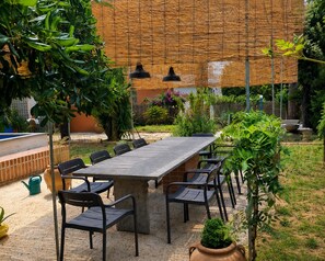 An outdoor patio with a long table and chairs, surrounded by greenery and a bamboo wall. - Chalet di Târa: 1970s-era villa with a private pool, within walking distance of the beach, and pet-friendly (Anzio)