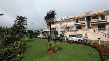 A residential building with a well-maintained lawn, potted plants, and a staircase leading to the upper floors.
