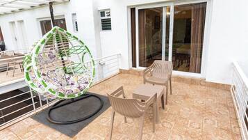 A balcony with a hanging chair, two tables, and chairs.