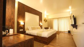 A hotel room with a large bed, wooden headboard, bedside lamps, and a flat-screen TV mounted on the wall.