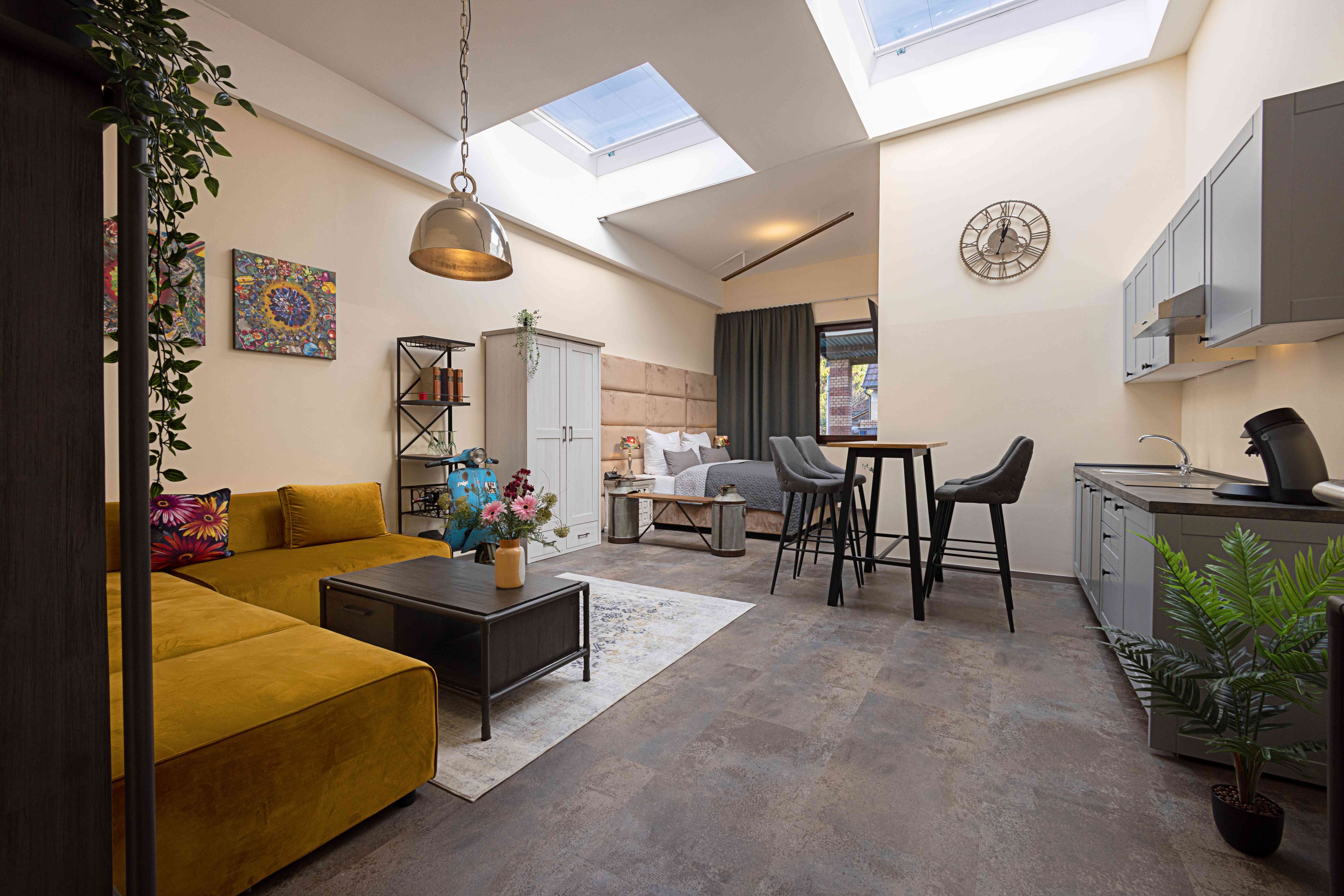Ein zeitgemäßer Wohnraum mit Sofa, Esstisch, Stühlen, Küchenzeile und Oberlicht.