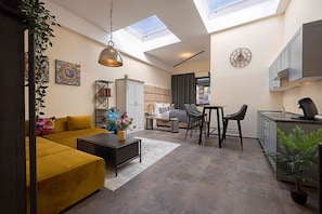 A modern living space with a sofa, dining table, chairs, a kitchen area, and a skylight. - Fabric-Apartments (Dettingen an der Erms)