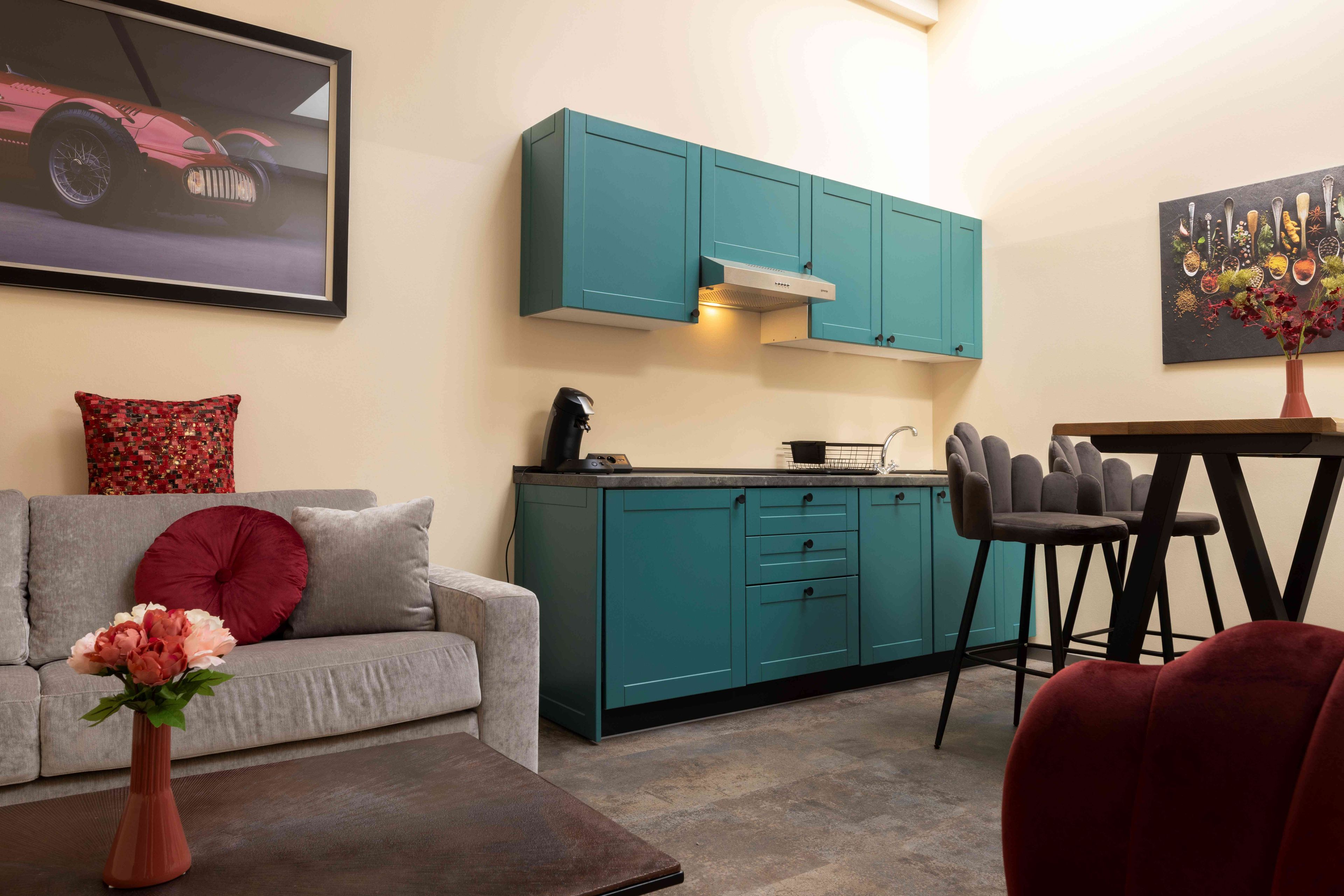 A modern kitchen with teal cabinets, a grey sofa, and a dining area with a table and chairs.