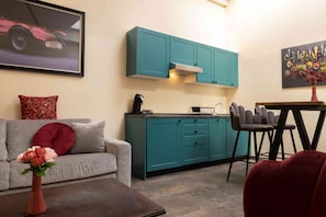 A modern kitchen with teal cabinets, a grey sofa, and a dining area with a table and chairs. - Fabric-Apartments (Dettingen an der Erms)
