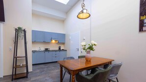 A compact kitchen with blue cabinets, a wooden dining table, and a hanging light fixture. - Fabric-Apartments (Dettingen an der Erms)