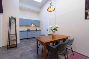 A compact kitchen with blue cabinets, a wooden dining table, and a hanging light fixture. - Fabric-Apartments (Dettingen an der Erms)