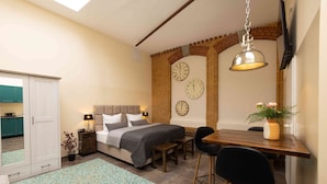 A bedroom with a bed, bedside tables, a desk, chairs, a potted plant, and a brick wall with clocks. - Fabric-Apartments (Dettingen an der Erms)