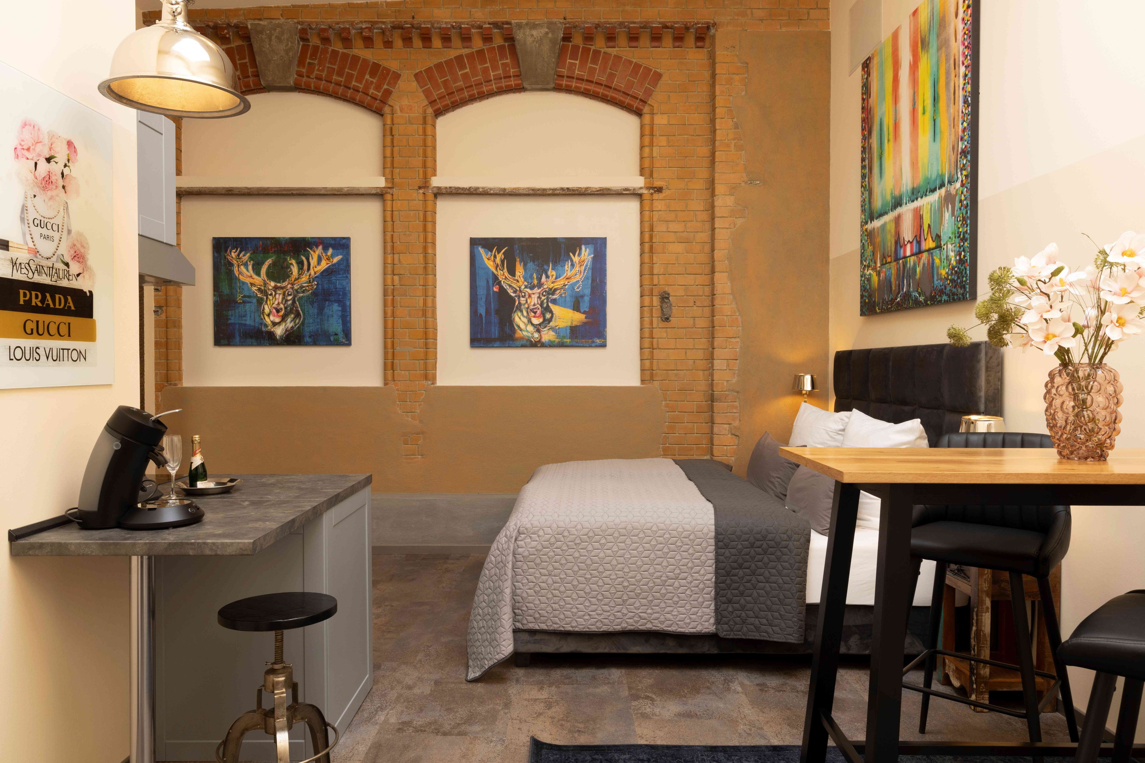 Habitació d'hotel moderna amb una llar de pedra, un llit, una taula de treball amb una màquina de cafè i obres d'art a les parets.
