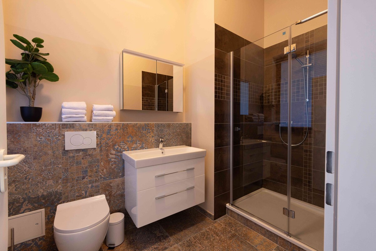 A modern bathroom with a glass-enclosed shower, a white sink, and a potted plant.