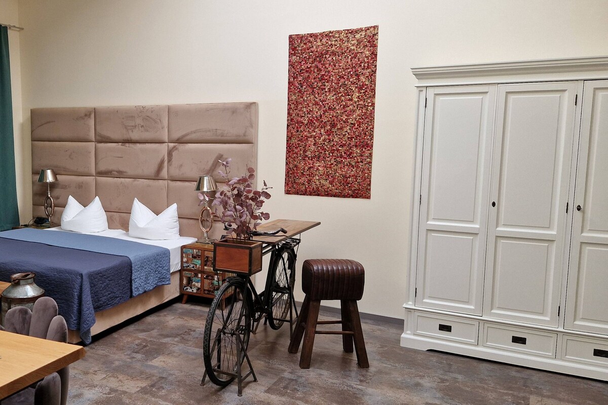 A bedroom with a bed, bedside table, lamp, and a bicycle.