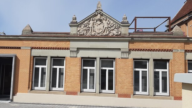 A building with a brick facade, large windows with shutters, and a decorative crest above the entrance. - Fabric-Apartments (Dettingen an der Erms)