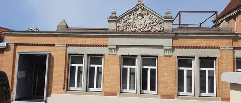 A building with a brick facade, large windows with shutters, and a decorative crest above the entrance.