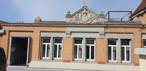A building with a brick facade, large windows with shutters, and a decorative crest above the entrance.