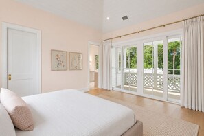 A bedroom with a large bed, a door, and a view of a balcony with a white fence. - Beach Escape, close to beach, new custom home (Isle Of Palms)