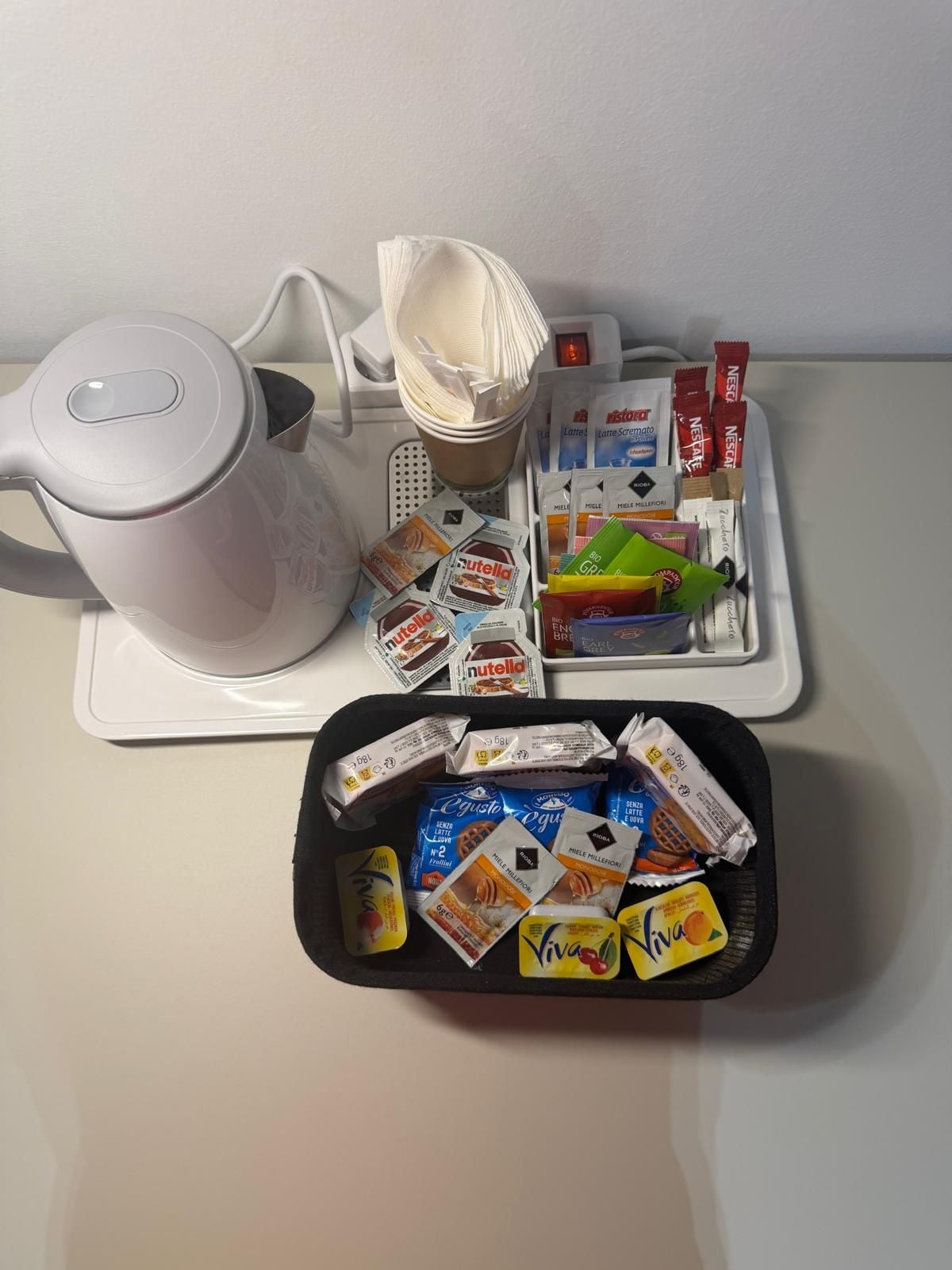 Una zona de cocina con cafetera, una bandeja con diferentes alimentos y una cesta de aperitivos envasados.