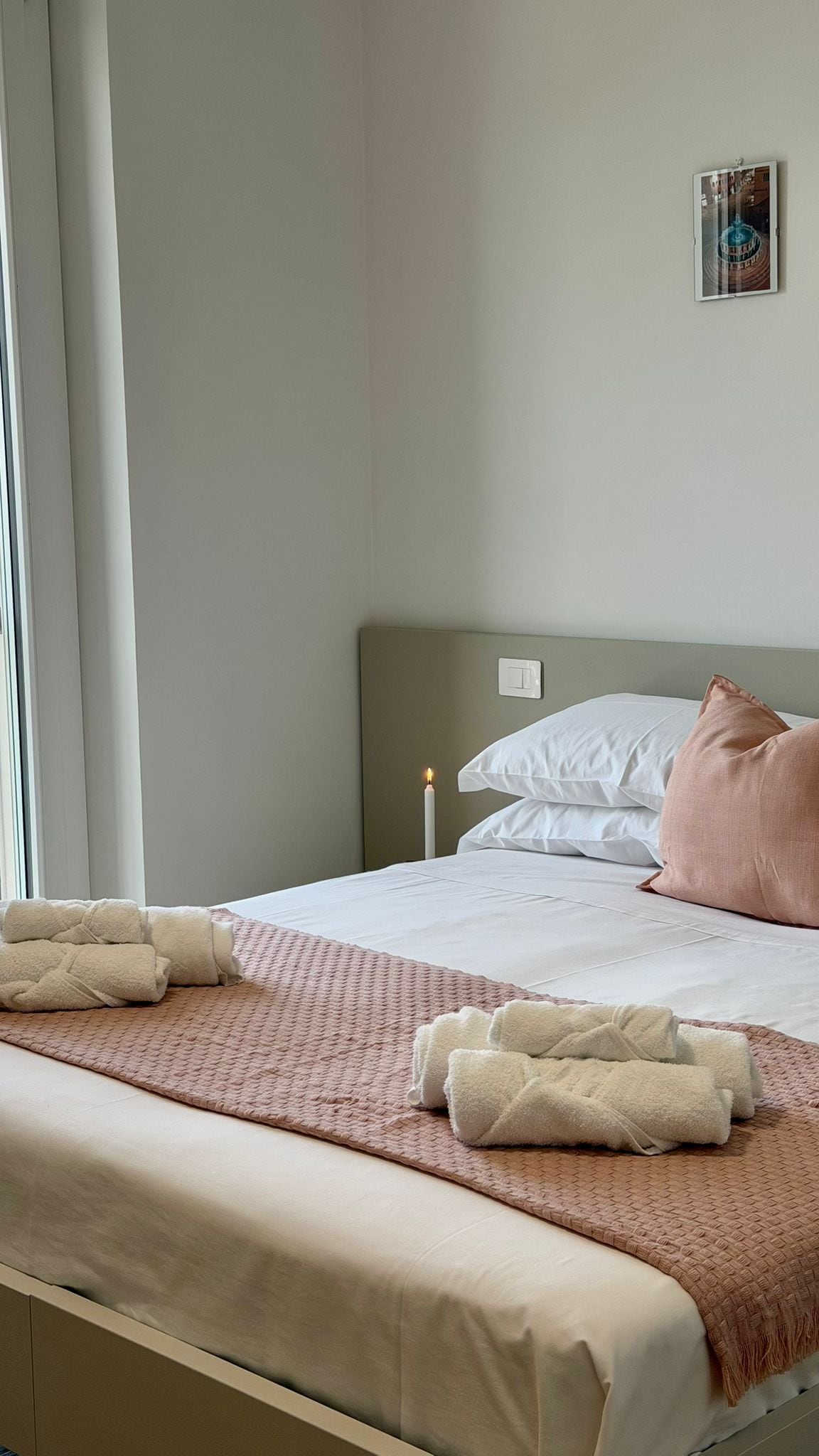 A hotel room with a bed, a bedside table with a candle, and a wall-mounted picture.