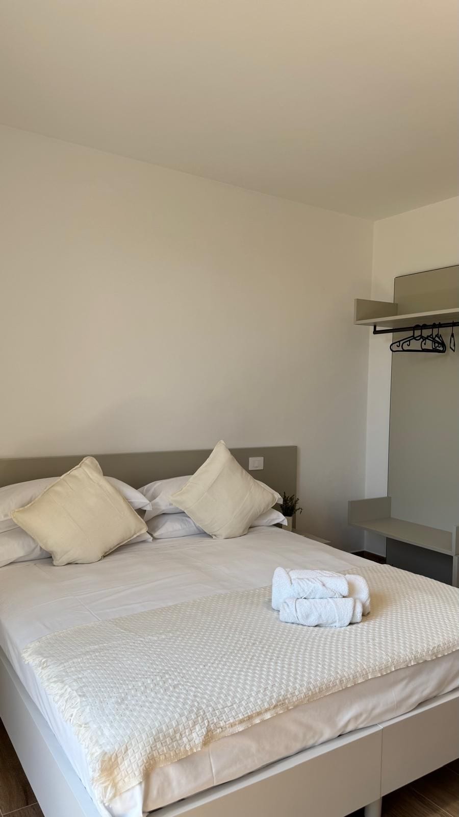 A bed with white bedding and pillows, a folded towel on the bed, and a nightstand with a plant.