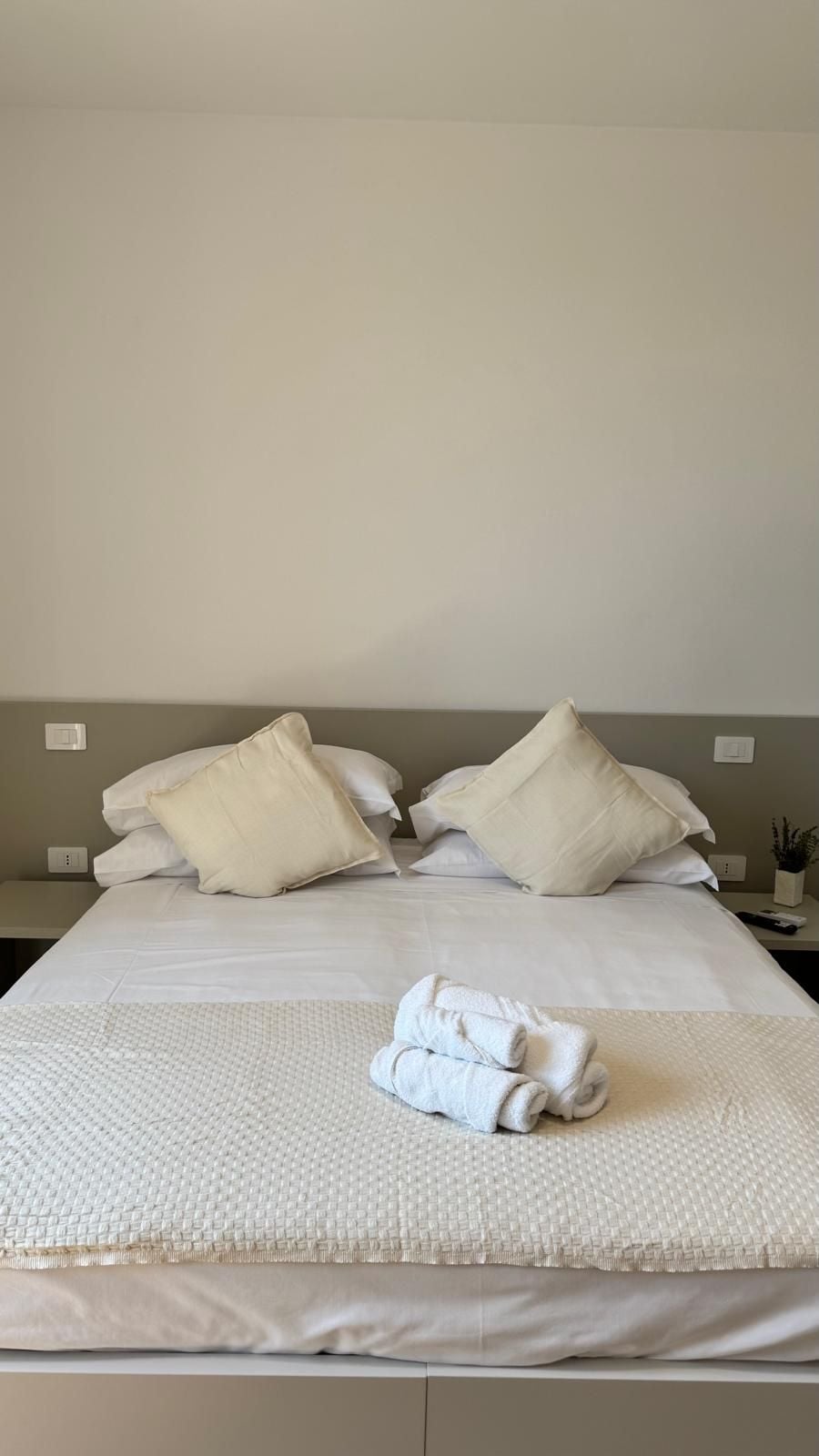 Una cama bien hecha con una colcha blanca texturizada, dos almohadas grandes y una toalla blanca doblada sobre la cama.
