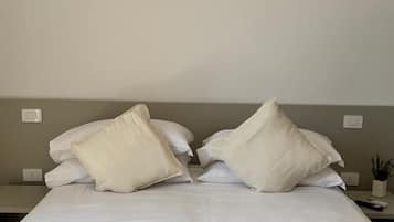 Una cama bien hecha con una colcha blanca texturizada, dos almohadas grandes y una toalla blanca doblada sobre la cama.