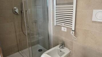 A bathroom with a glass-enclosed shower, a bidet, and a toilet.