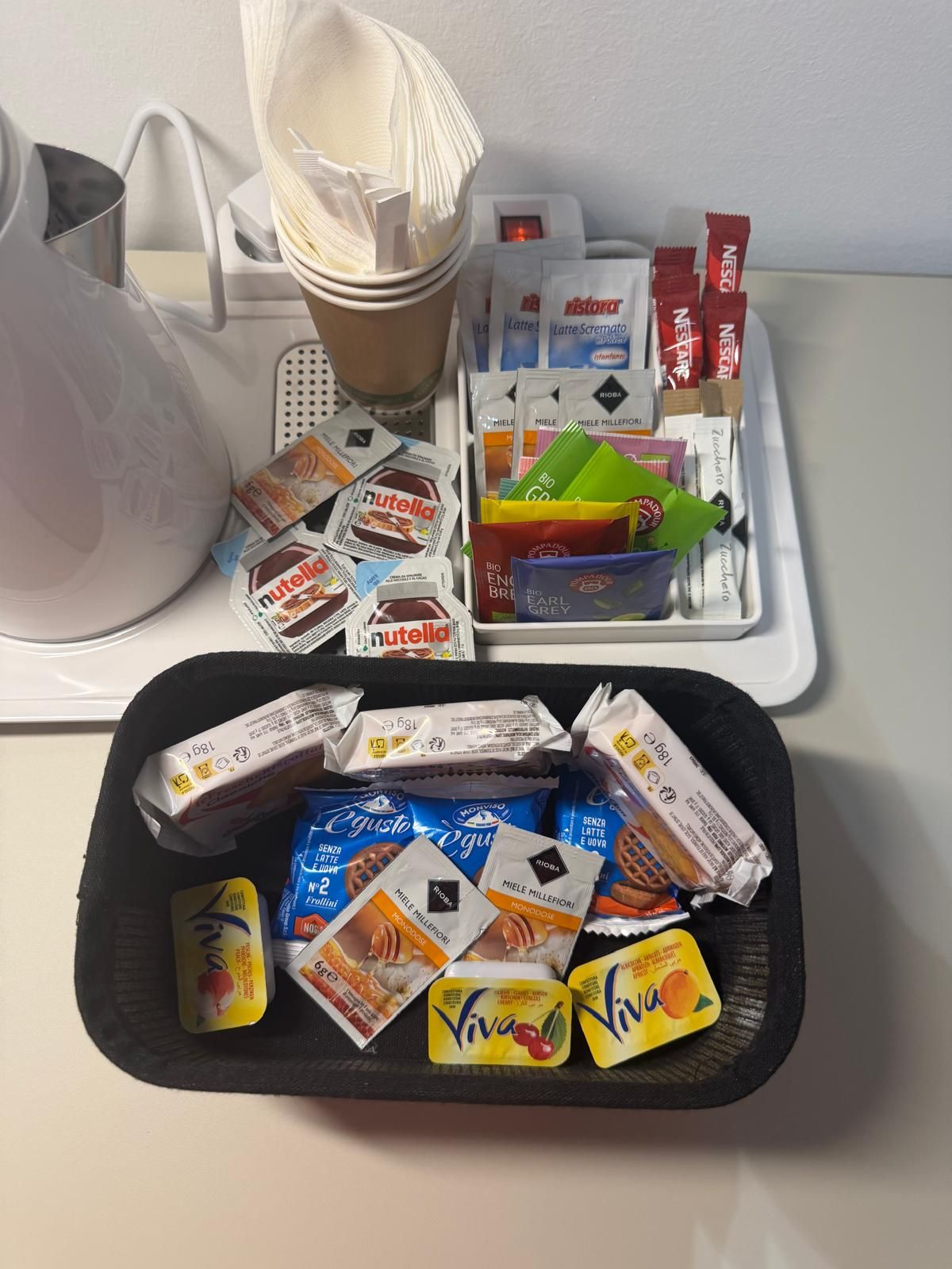 Uma bandeja com diversos alimentos, incluindo Nutella, cápsulas de café e lanches embalados.