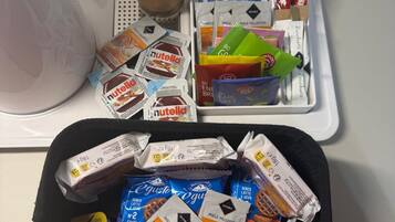 Uma bandeja com diversos alimentos, incluindo Nutella, cápsulas de café e lanches embalados.