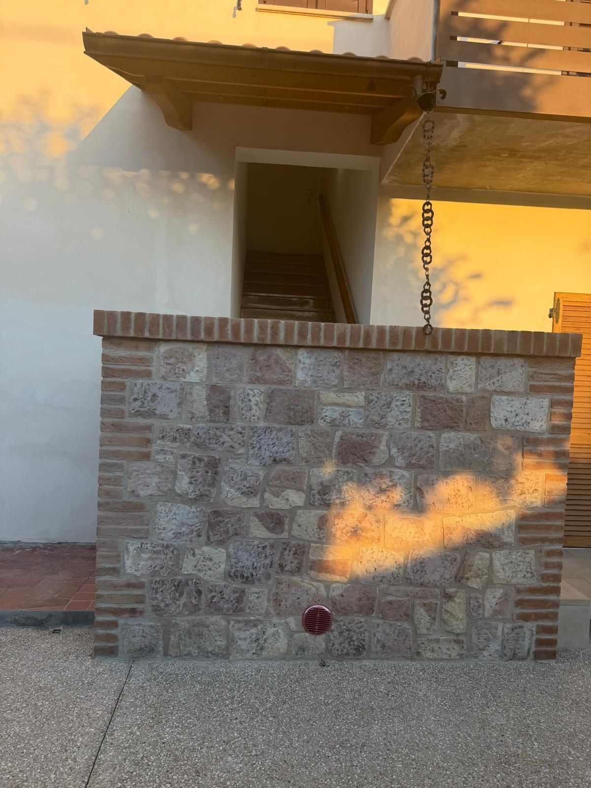 Um muro de pedra com um portão de metal, um hidrante vermelho e uma porta de madeira ao fundo.