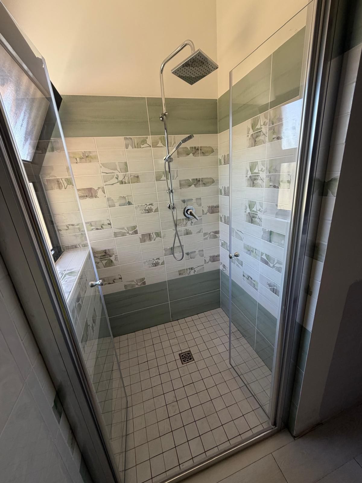 A glass-enclosed shower with a handheld showerhead and a wall-mounted faucet.