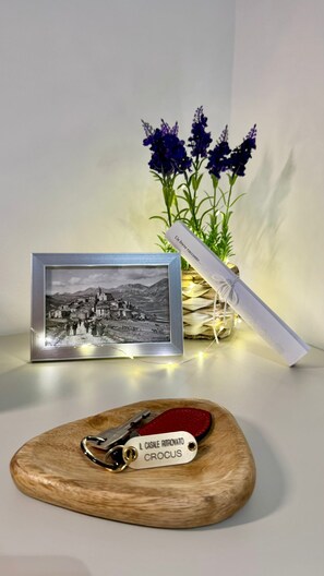 A framed photograph of a village, a wooden plaque with a key, and a vase with purple flowers. - Il Casale Ritrovato (Perugia)