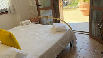 A bedroom with a bed, a bedside table, a window with curtains, and an open door leading to an outdoor area.