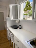Cocina compacta con encimera blanca, microondas integrado, lavamanos y ventana con vistas a zonas verdes.
