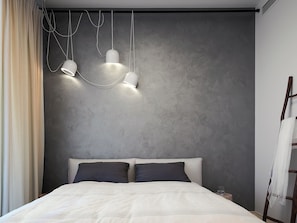 A modern bedroom with a bed, two bedside lamps, and a plain wall.