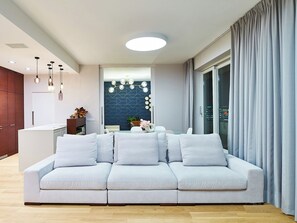 Un soggiorno moderno con un divano, lampade a sospensione e vista sulla città attraverso la finestra.