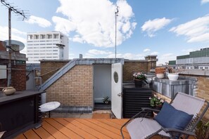 Una terraza en la azotea con un muro de ladrillo, una puerta pequeña y una zona de estar con mesa y sillas.
