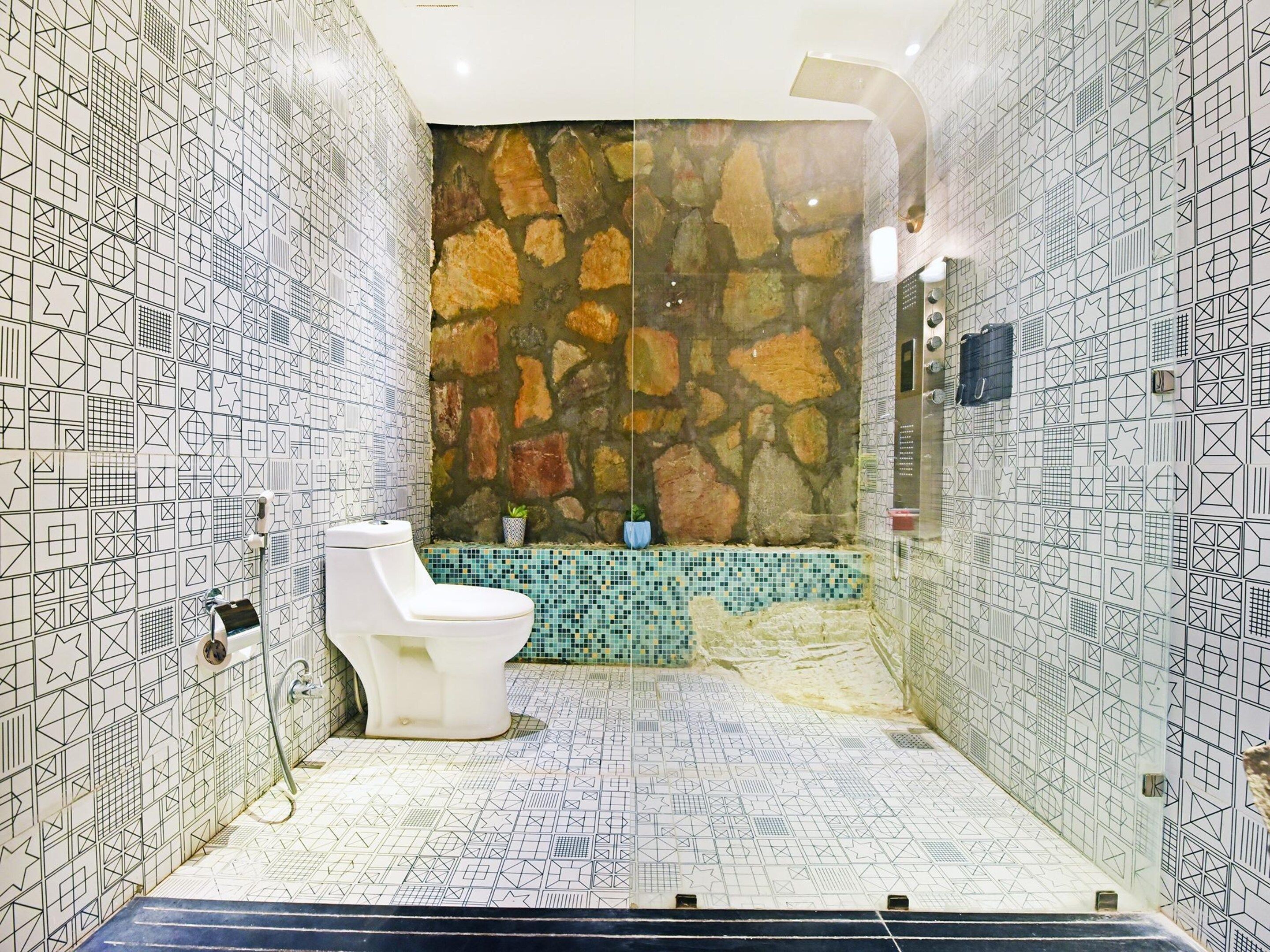 Casa de banho com sanita branca, parede de pedra e azulejos estampados.
