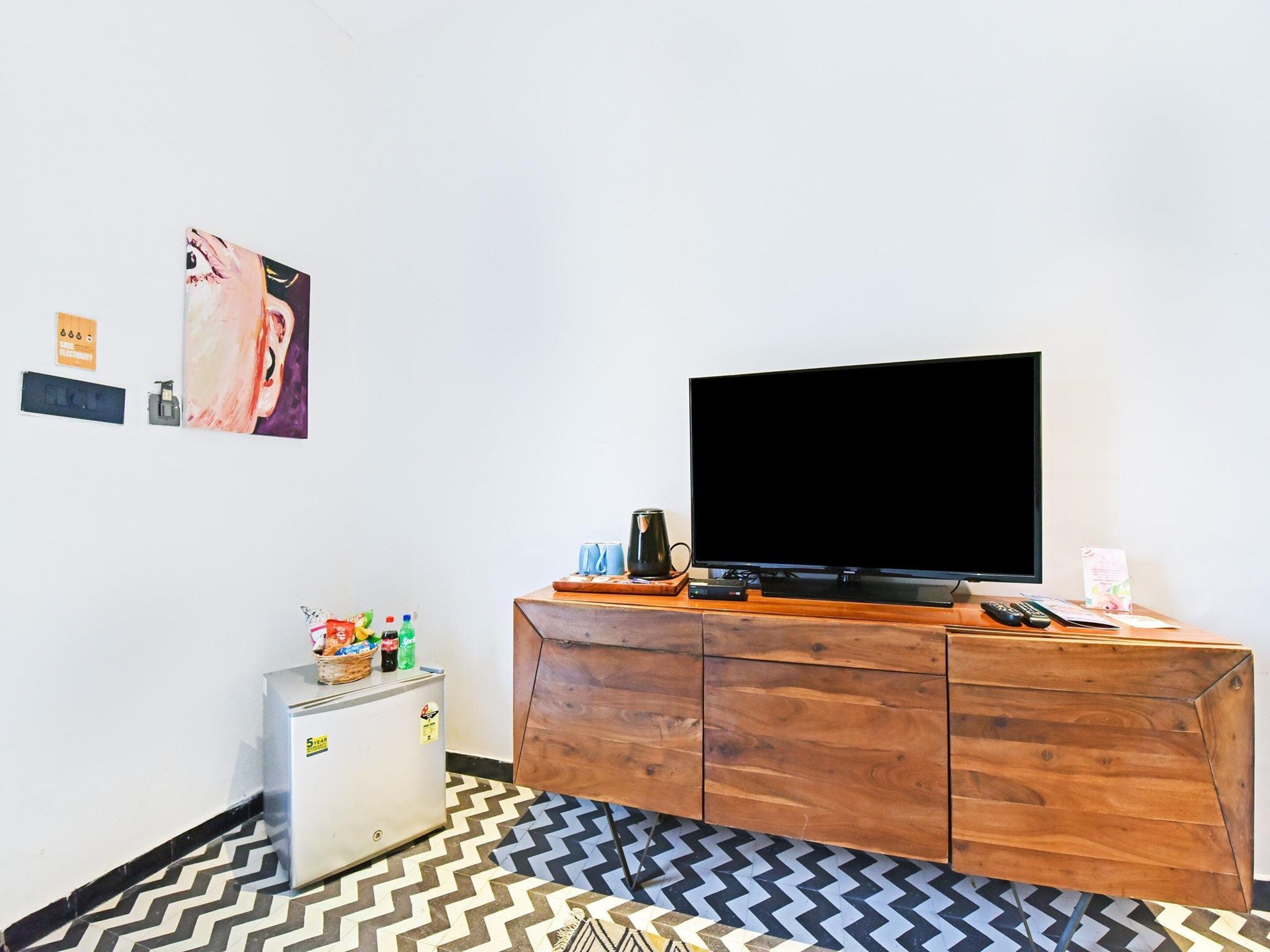 A room with a television on a wooden cabinet, a small refrigerator, and a patterned floor.