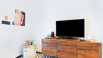 A room with a television on a wooden cabinet, a small refrigerator, and a patterned floor.
