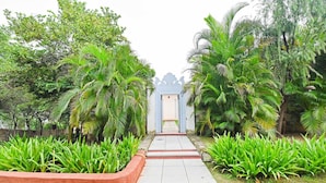 Un chemin menant à un bâtiment à l’architecture traditionnelle, entouré d’une végétation luxuriante et de palmiers.