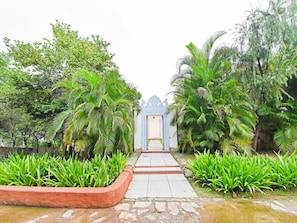 Un sendero conduce a un edificio de estilo arquitectónico tradicional, rodeado de abundante vegetación y palmeras.