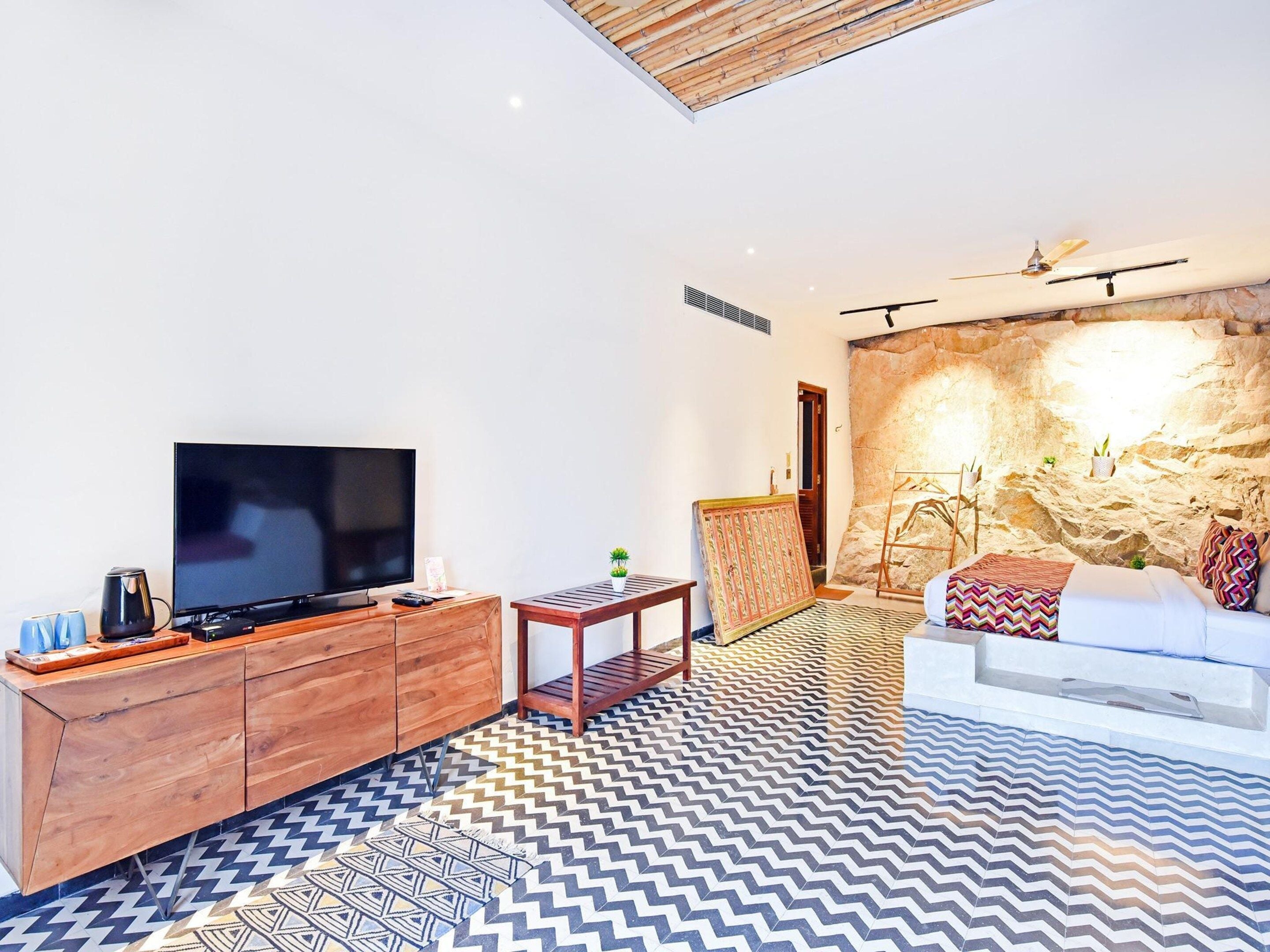 Ein modernes Wohnzimmer mit einem Flachbildfernseher, Holzmöbeln, einem gemusterten Boden und einer Steinwand.