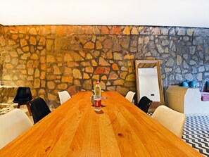 A conference room with a wooden table, white chairs, a stone wall, and a large mirror.