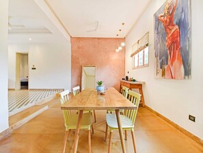Un comedor con una mesa y sillas de madera, una planta en maceta y un cuadro en la pared.